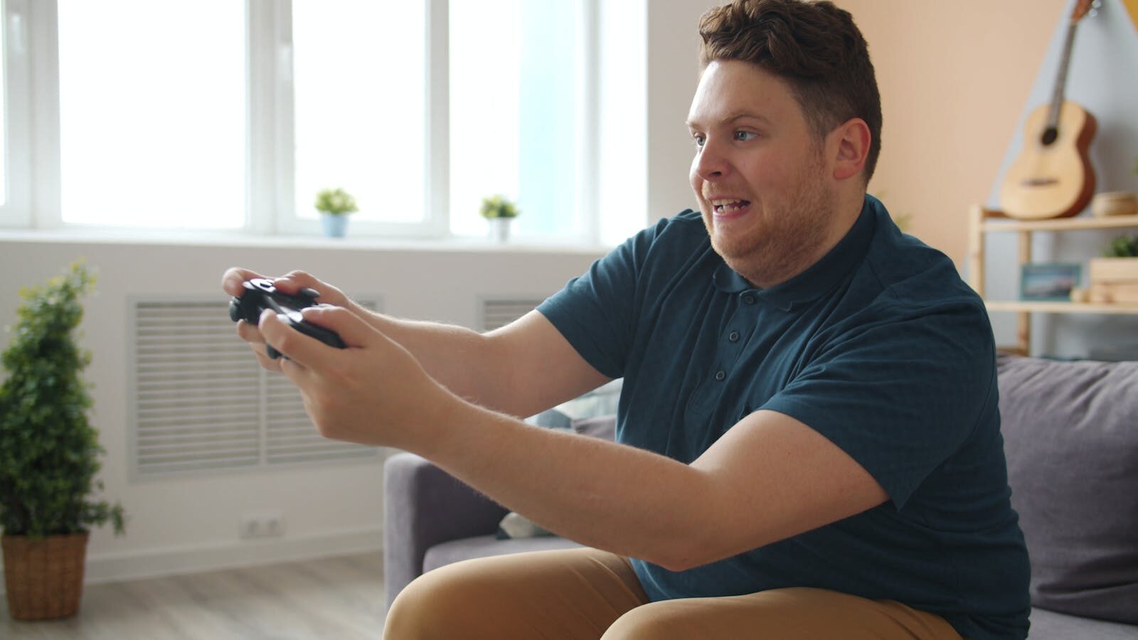 Happy adult engaged in video gaming, sitting on a couch indoors.